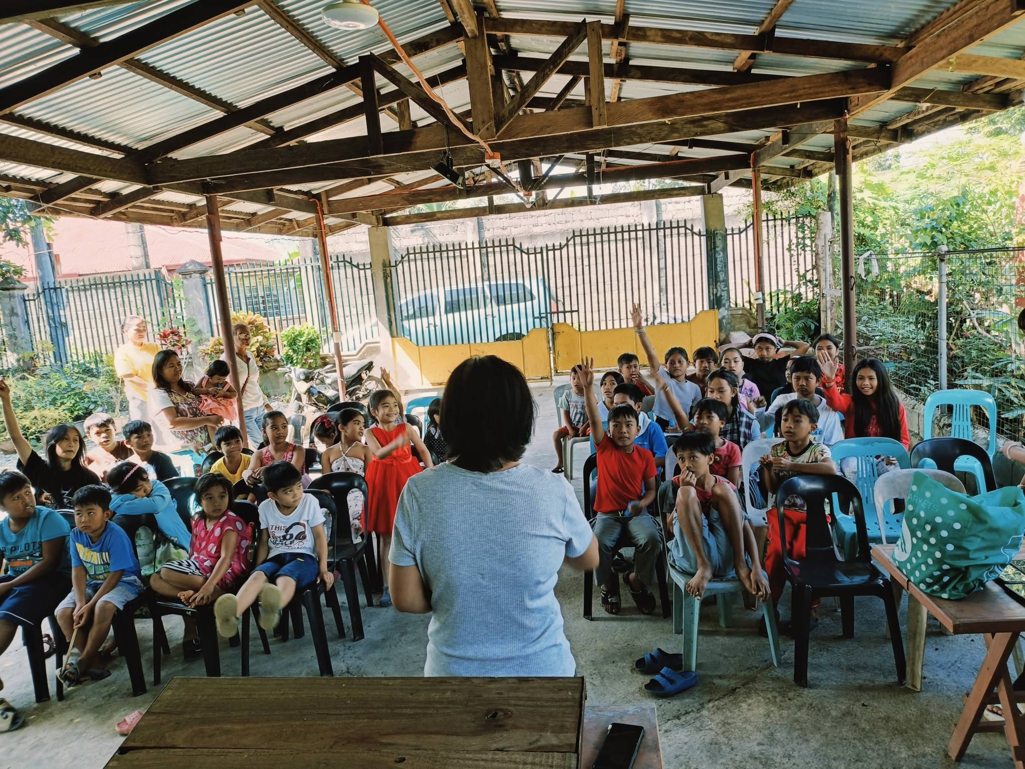 A volunteer teacher leading a lively Bible lesson as children raise their hands to answer
