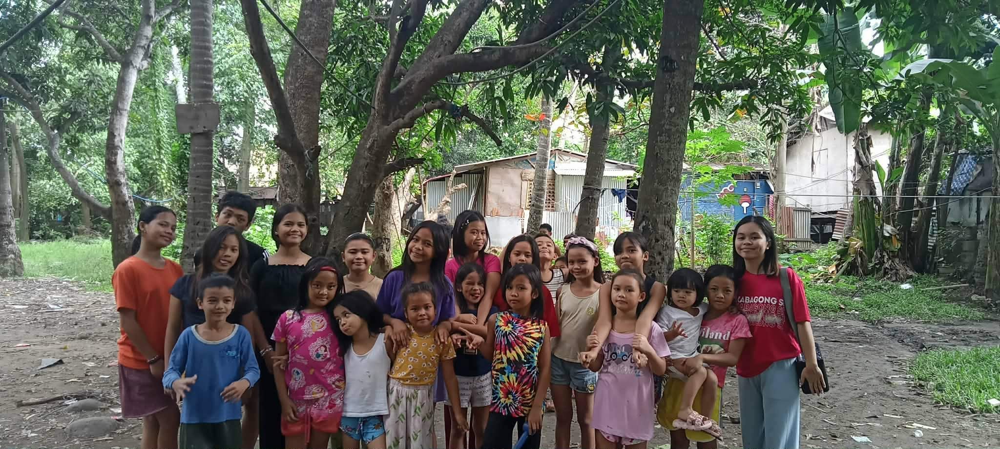 A large group of children gathered under the trees during a Marilog outreach